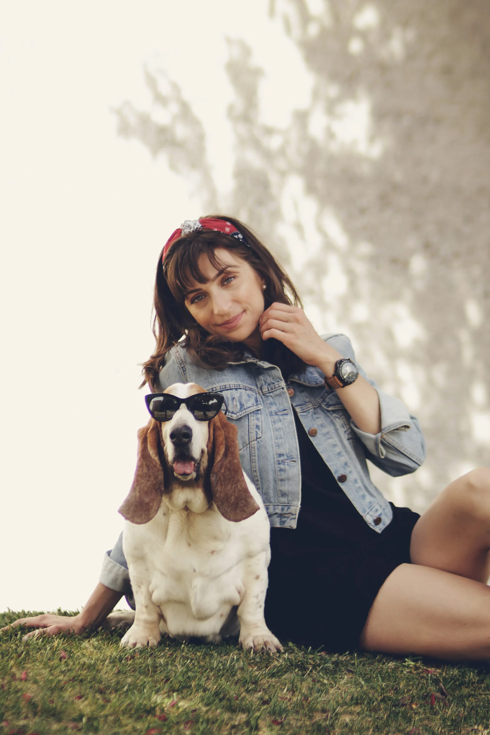 A woman sitting calmly beside a basset hound on a wooden deck, both facing forward in quiet companionship.